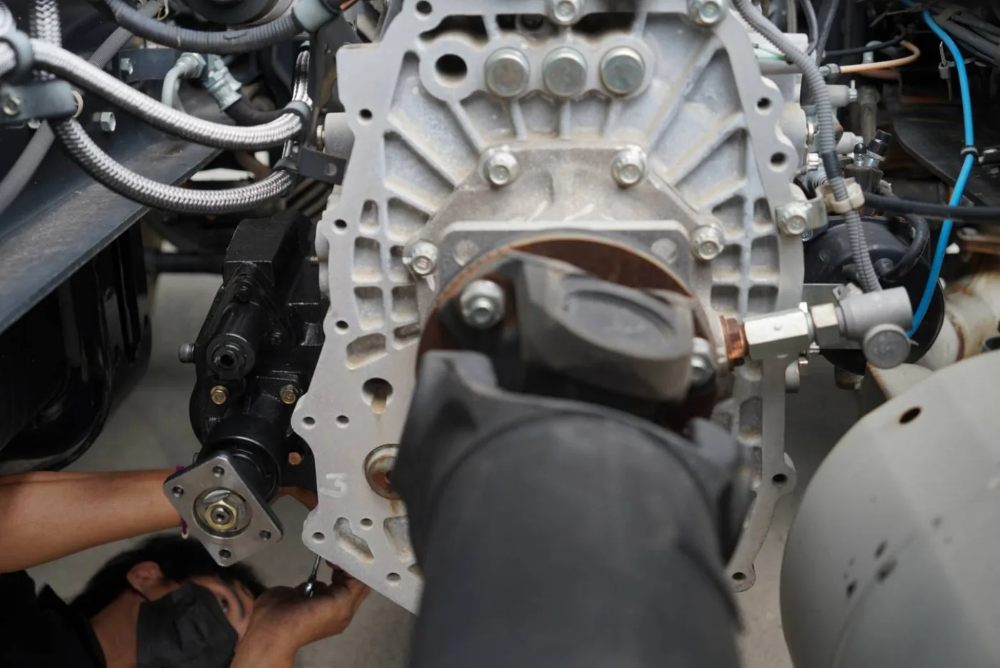VPS technician fitting a PTO and its shift mechanism under a truck gearbox